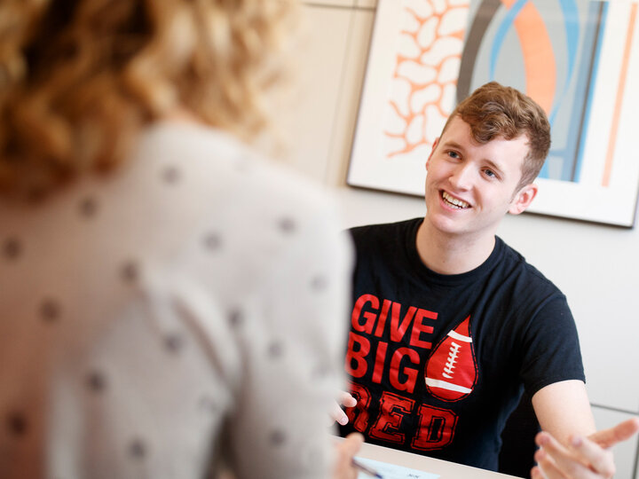 A student sitting at an office desk talking to a financial aid counselor